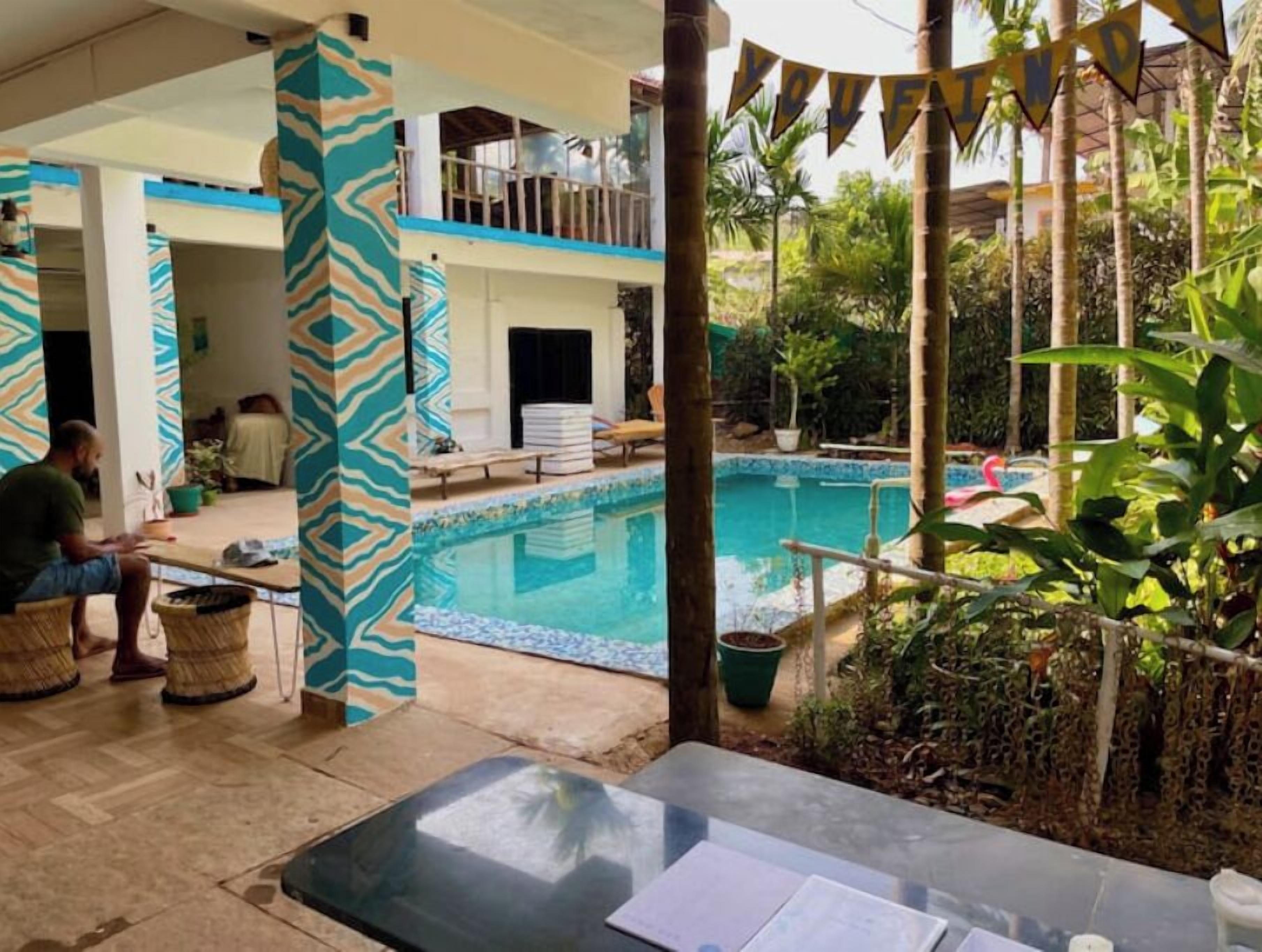 A poolside area with a clear view of the pool, a covered seating area, and a person sitting at a table.