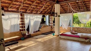 A room with a wooden floor, a bed with a red blanket, a bench, and a window with a view of greenery. - Sky Studio Apartment 02 Blue Sky Rentals
 (Canacona)