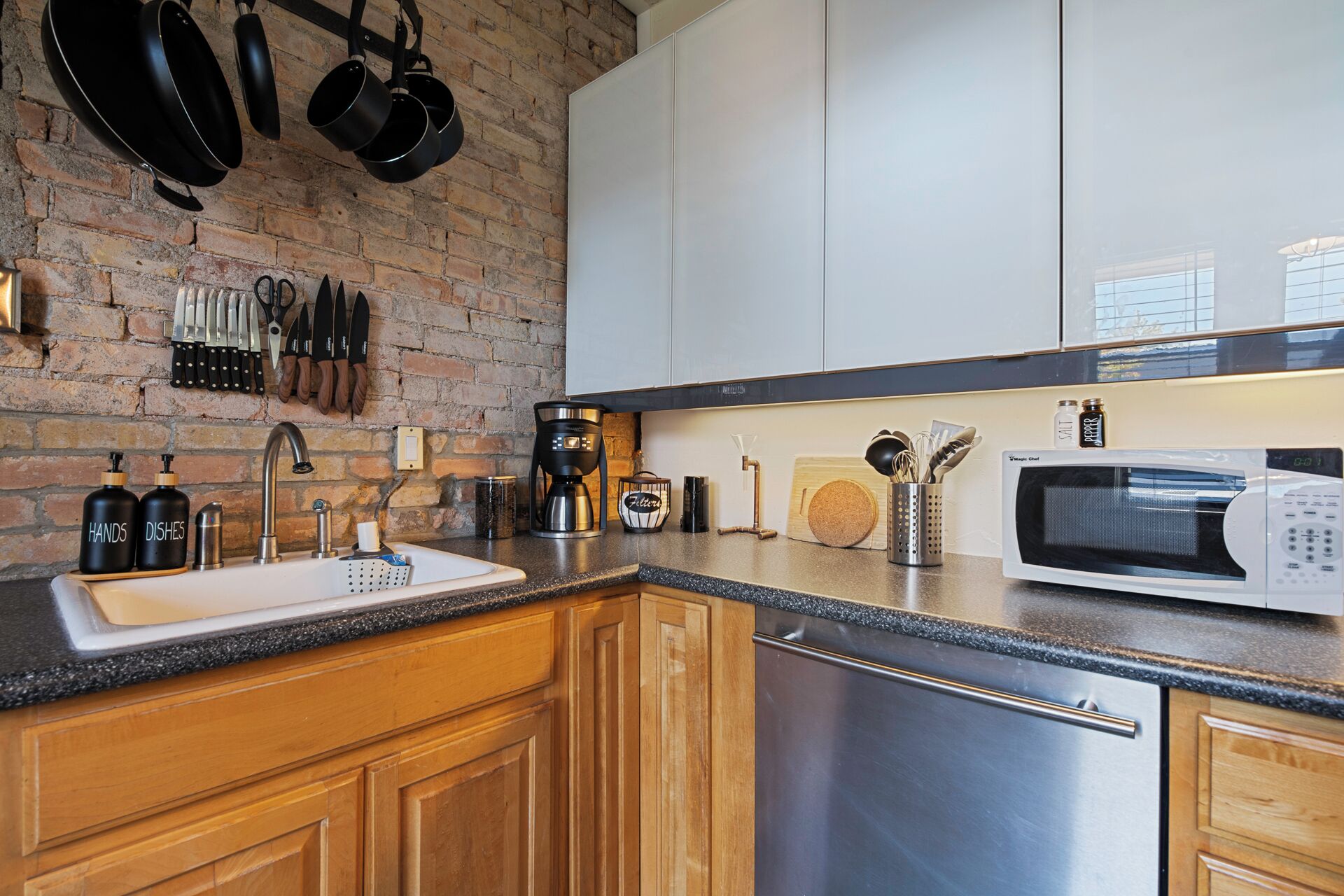 A modern kitchen with a brick wall, stainless steel appliances, wooden cabinets, and a granite countertop.