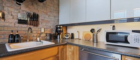 A modern kitchen with a brick wall, stainless steel appliances, wooden cabinets, and a granite countertop.