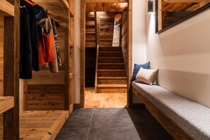 A wooden interior with a staircase, a bench, and a closet with hanging clothes.