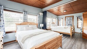 Ein Doppelzimmer mit zwei hölzernen Betten, einer Holzbalkendecke und großen Fenstern mit Vorhängen.