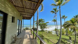 A wooden deck with a view of the ocean and palm trees. - Charming oceanfront cabin with stunning views, private terrace, and beach access (Santa Marta)