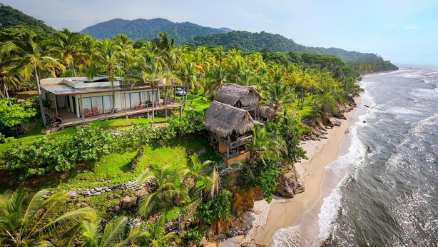 A coastal property with a modern house and a traditional hut, surrounded by lush greenery and a beach. - Charming oceanfront cabin with stunning views, private terrace, and beach access (Santa Marta)