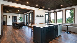 A spacious kitchen with a large island, wooden flooring, and large windows offering a view of the outdoors. - 3-Level Luxury Cabin w/ Indoor Pool, Game Loft & Stunning Views (Sevierville)