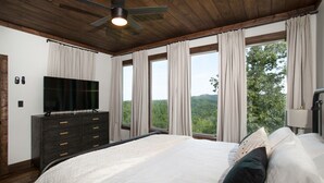 A bedroom with a large bed, a TV on a dresser, and a view of the outdoors. - 3-Level Luxury Cabin w/ Indoor Pool, Game Loft & Stunning Views (Sevierville)