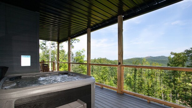 A hot tub on a wooden deck with a view of a forested mountain range. - 3-Level Luxury Cabin w/ Indoor Pool, Game Loft & Stunning Views (Sevierville)