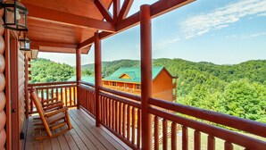 Une terrasse en bois offrant une vue sur un chalet doté d’un toit végétalisé, lui-même entouré de collines boisées.