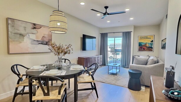 A modern living room with a dining area, a ceiling fan, and a large window with curtains.