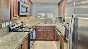 A modern kitchen with wooden cabinets, stainless steel appliances, and a window with a view.