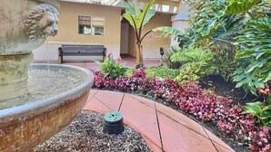 A courtyard with a fountain, a bench, and lush greenery.