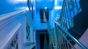 A narrow hallway with a blue wall, a staircase with metal railings, and a door at the end. - Lexaren Luxury Apartments (Asaba)
