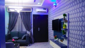 A modern living room with a sofa, TV, and decorative wall. - Lexaren Luxury Apartments (Asaba)