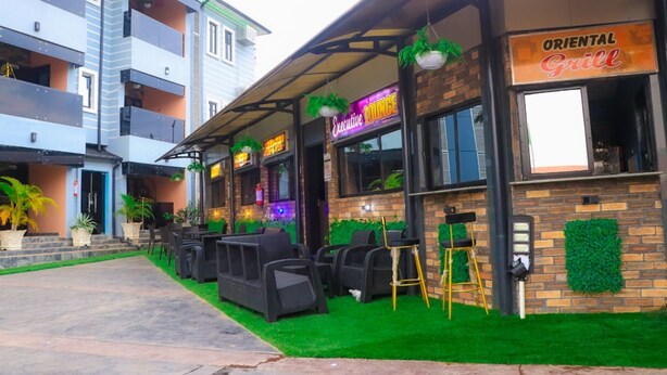 A restaurant with outdoor seating, a neon sign, and a brick facade. - Lexaren Luxury Apartments (Asaba)