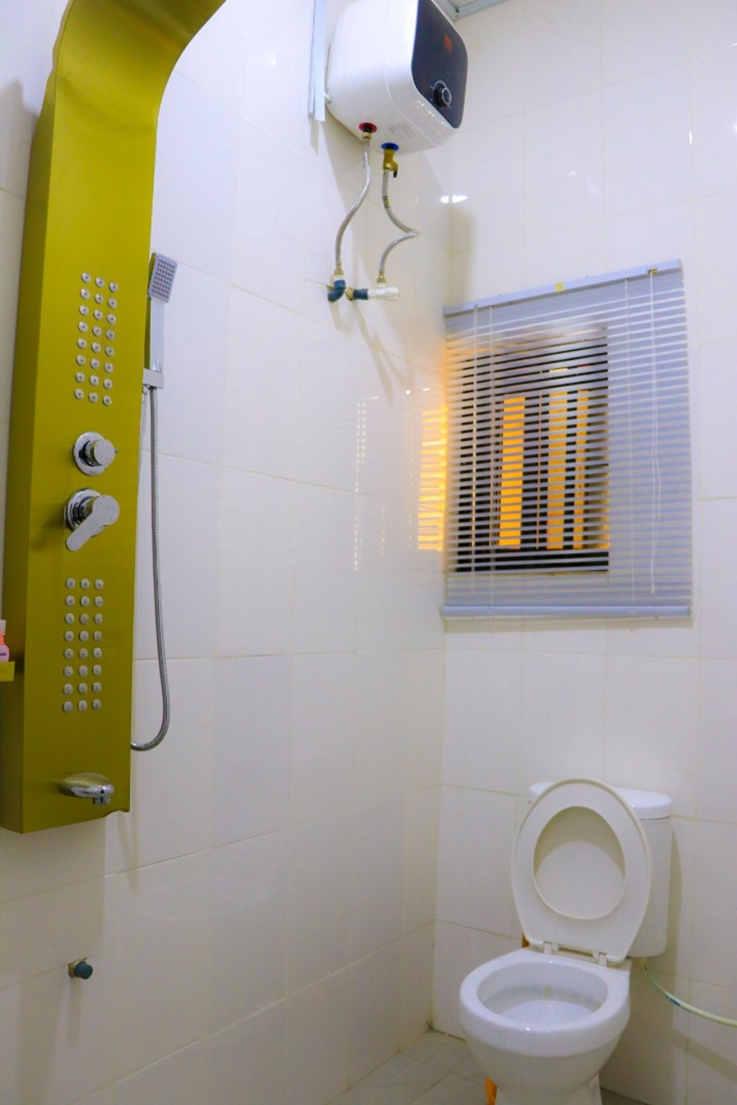 A bathroom with a shower, toilet, and a window with blinds.
