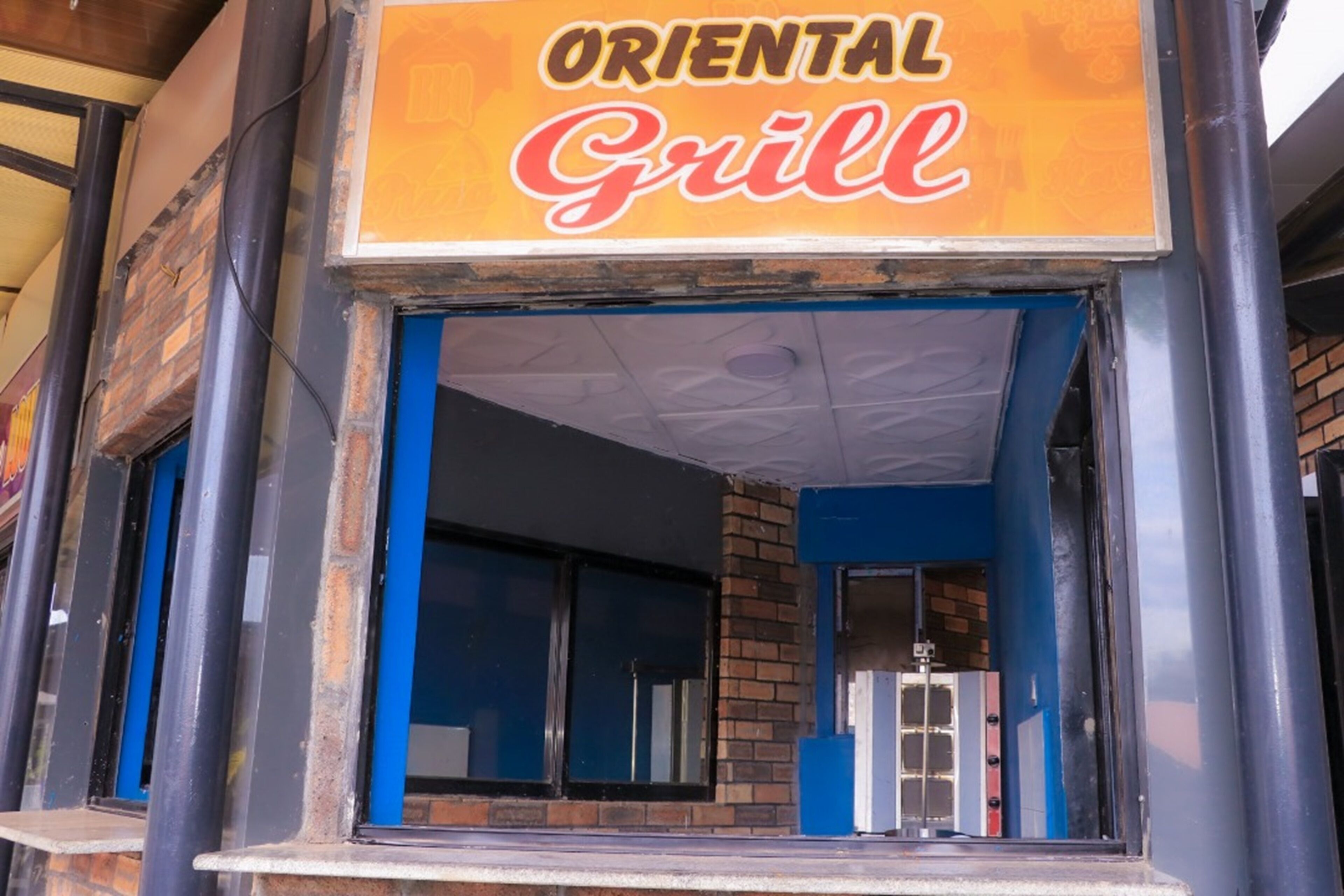Une enseigne de restaurant indiquant « ORIENTAL Grill », avec une façade en briques et des touches de couleur bleue.