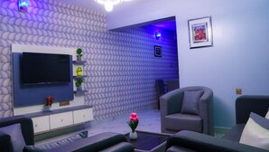 A modern living room with a flat-screen TV, comfortable seating, decorative wall panels, and ambient lighting. - Lexaren Luxury Apartments (Asaba)