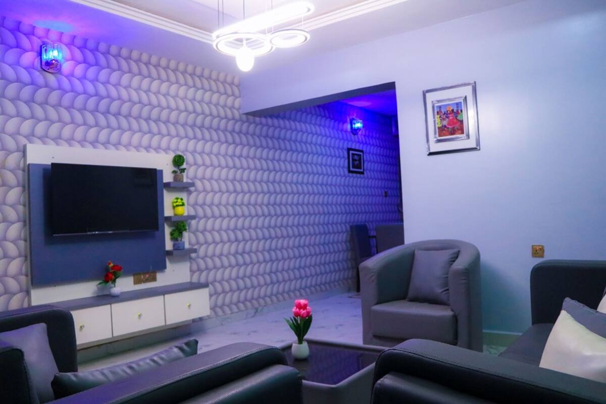 Una sala de estar moderna con un televisor de pantalla plana, asientos cómodos, paneles decorativos en la pared e iluminación ambiental.