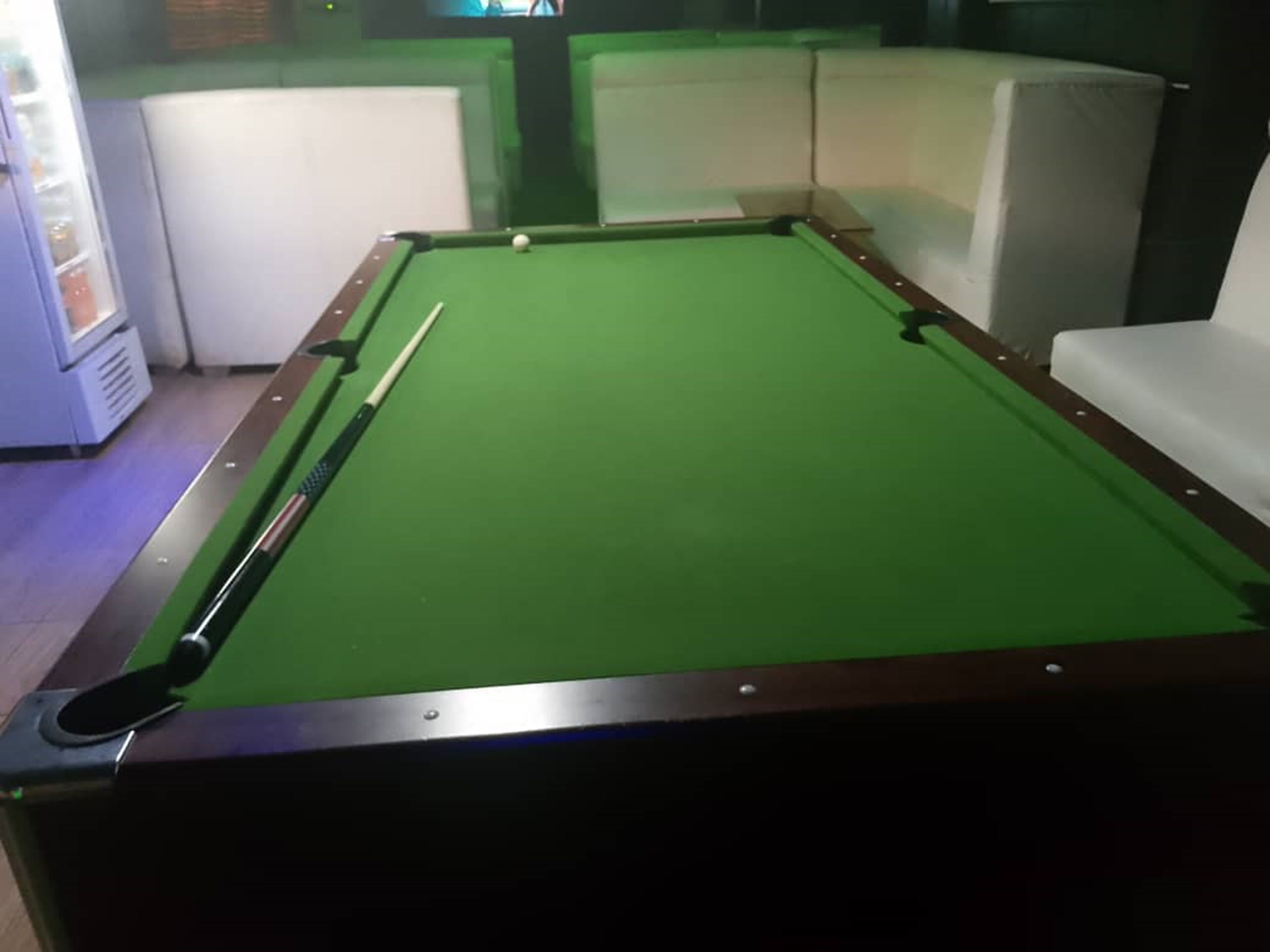 A pool table with a green felt surface, surrounded by white cushioned seating.
