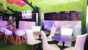 A seating area with white chairs and tables, surrounded by green artificial grass and a wall with various emblems. - Lexaren Luxury Apartments (Asaba)