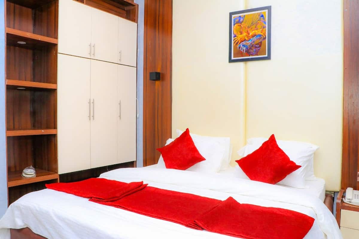 Habitación de hotel con cama, almohadas rojas, una manta roja, un armario de madera y un cuadro en la pared.