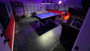 Una habitación con mesa de billar, dardos y un cartel de 'Street Fighter II'.