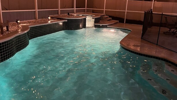 Una piscina interior con borde de azulejos, un jacuzzi y una zona de estar con una pérgola.