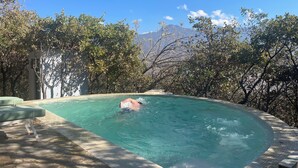 Ein Schwimmbecken mit einer darin schwimmenden Person, umgeben von Bäumen und Bergen im Hintergrund.