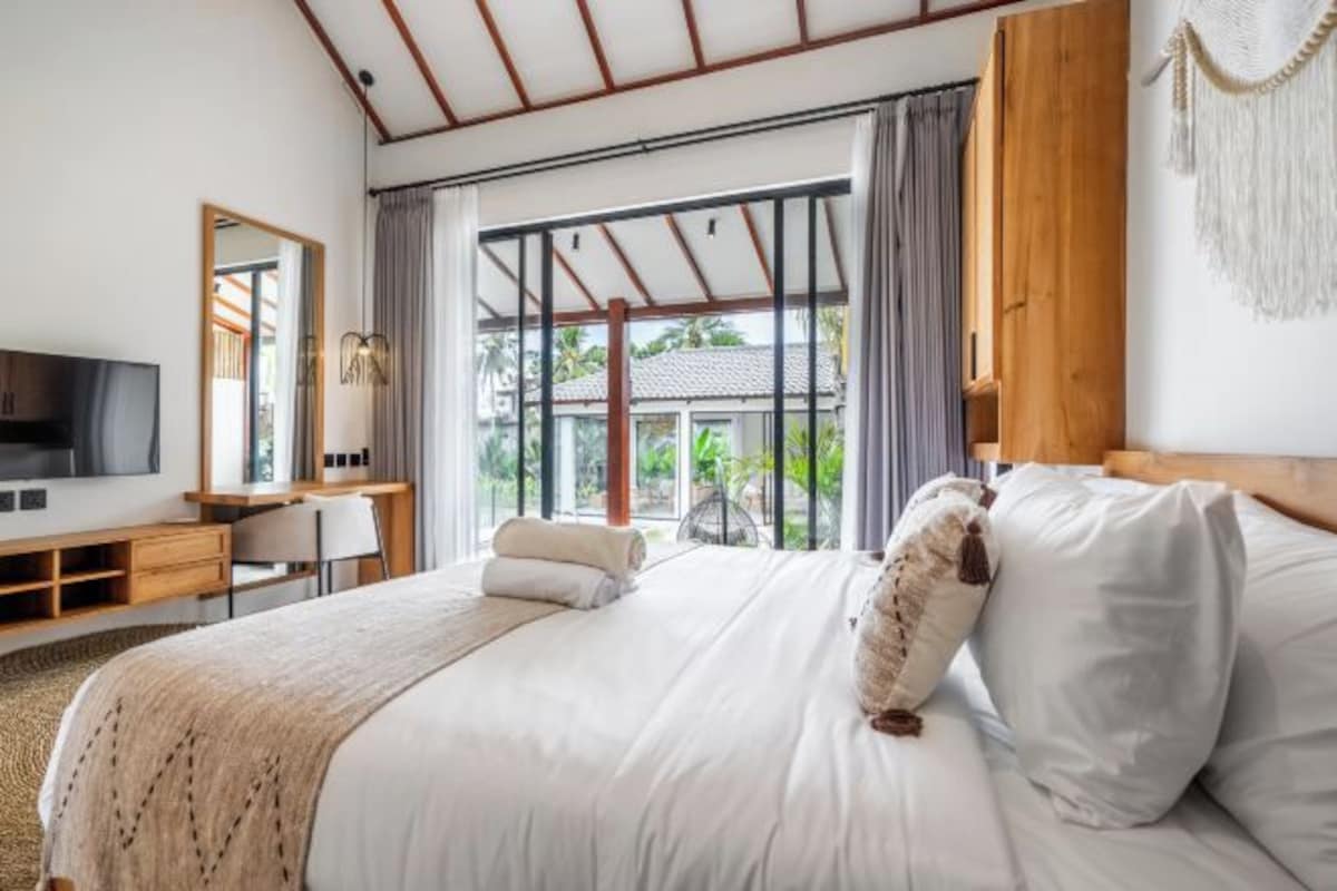 A bedroom with a large bed, a TV, a desk, and a window with curtains.