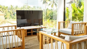 A modern living area with a glass coffee table, wooden furniture, and a large TV. - Rice Field Villa Ubud (Tegallalang)