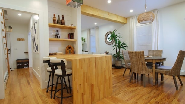 A modern kitchen with wooden flooring, a central island with stools, and a dining area with wicker chairs.