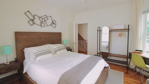 A bedroom with a large bed, a desk, a chair, a mirror, and a staircase leading to another room.