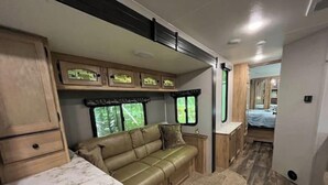 Ein kompakter Wohnraum in einem Wohnmobil mit Küchenzeile, einer Sitzecke und einem Bett.