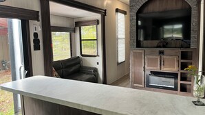 A modern RV kitchen with a stone fireplace, a built-in TV, and a seating area. - Modern RV come “GLAMP” in style. (Grand Rapids)