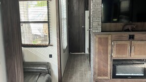 A compact RV interior with a kitchenette, a built-in TV, and a seating area. - Modern RV come “GLAMP” in style. (Grand Rapids)