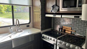 A compact kitchen with a sink, stainless steel appliances, a microwave, and a view of the outdoors. - Modern RV come “GLAMP” in style. (Grand Rapids)