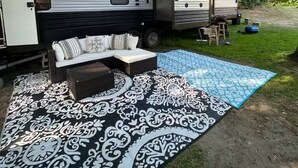 A mobile home with a porch area featuring a sofa and a patterned rug. - Modern RV come “GLAMP” in style. (Grand Rapids)