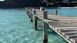 Eine hölzerne Pier, die sich in klares türkisfarbenes Wasser erstreckt, mit Bäumen und Gebäuden im Hintergrund.