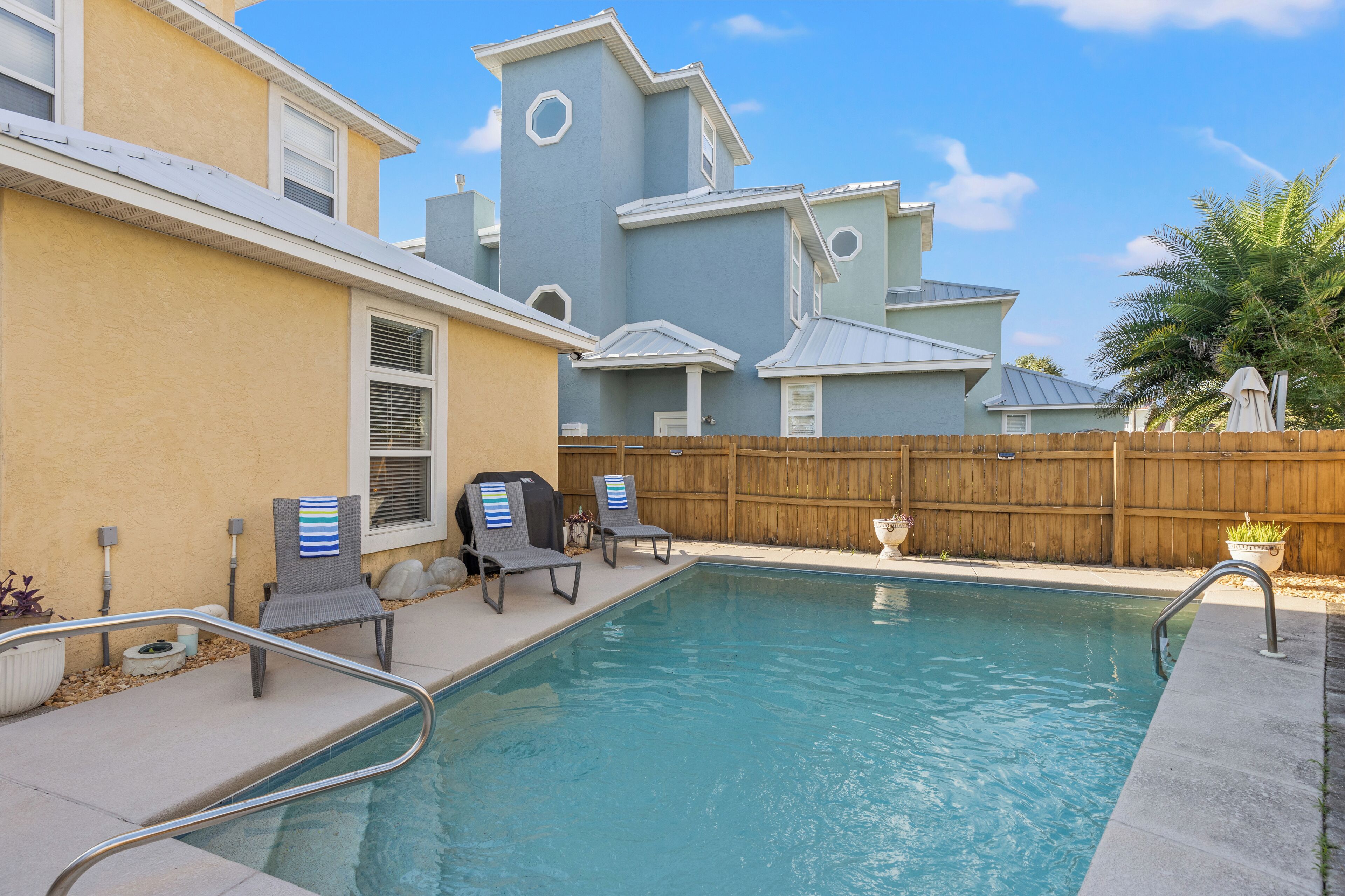A swimming pool with two lounge chairs and a wooden fence in the background.