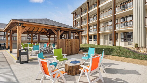 An outdoor seating area with white and colorful chairs, a wooden table, and a covered pavilion.
