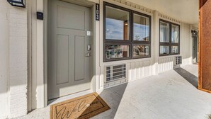A building entrance with a grey door, large windows, and a number '103' sign.