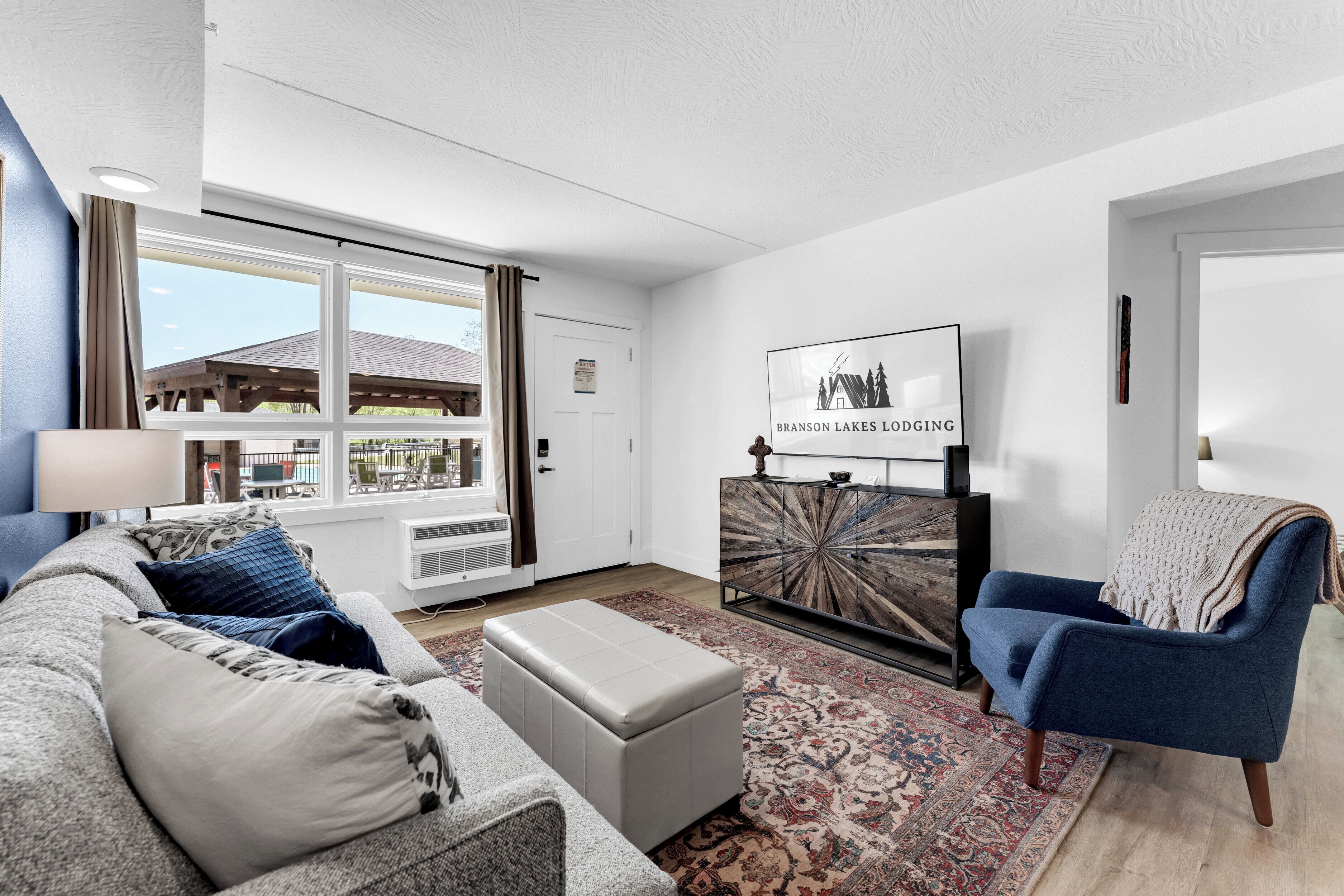 Un soggiorno moderno con un divano grigio, una poltrona blu, un tappeto decorato e un quadro di Branson Lakes Lodging.