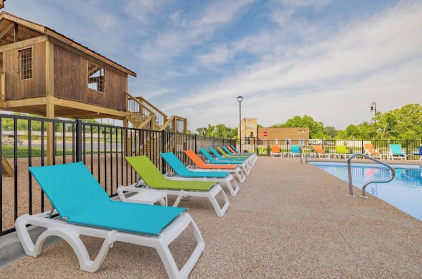A poolside area with multiple lounge chairs and a wooden building in the background.