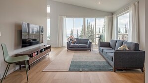 Un salon moderne avec un grand téléviseur à écran plat, un canapé gris, un fauteuil vert et un plancher en bois.