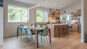 Une cuisine moderne dotée d’un îlot central, de grandes fenêtres et d’un coin repas avec des chaises.