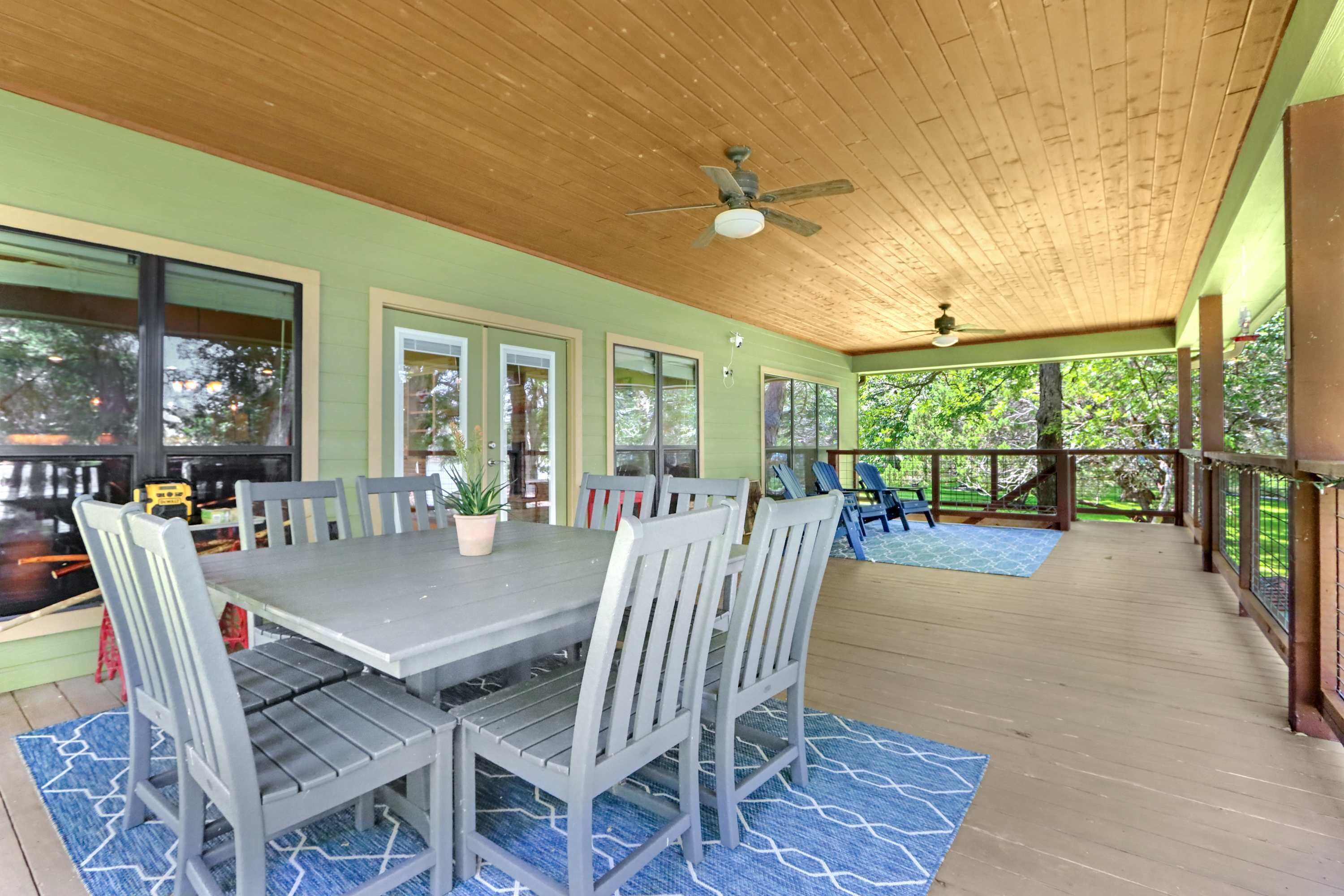 A covered outdoor dining area with a table and chairs, large windows, and a ceiling fan.