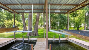 Une terrasse en bois couverte, avec une piscine, entourée d’arbres et d’une pelouse.