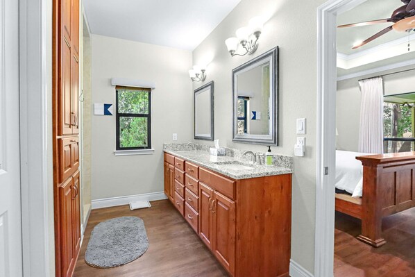 A bathroom with wooden cabinets, a granite countertop, a large mirror, and a ceiling fan. - Beautiful Lakefront Cabin Something For Everyone (New Braunfels)