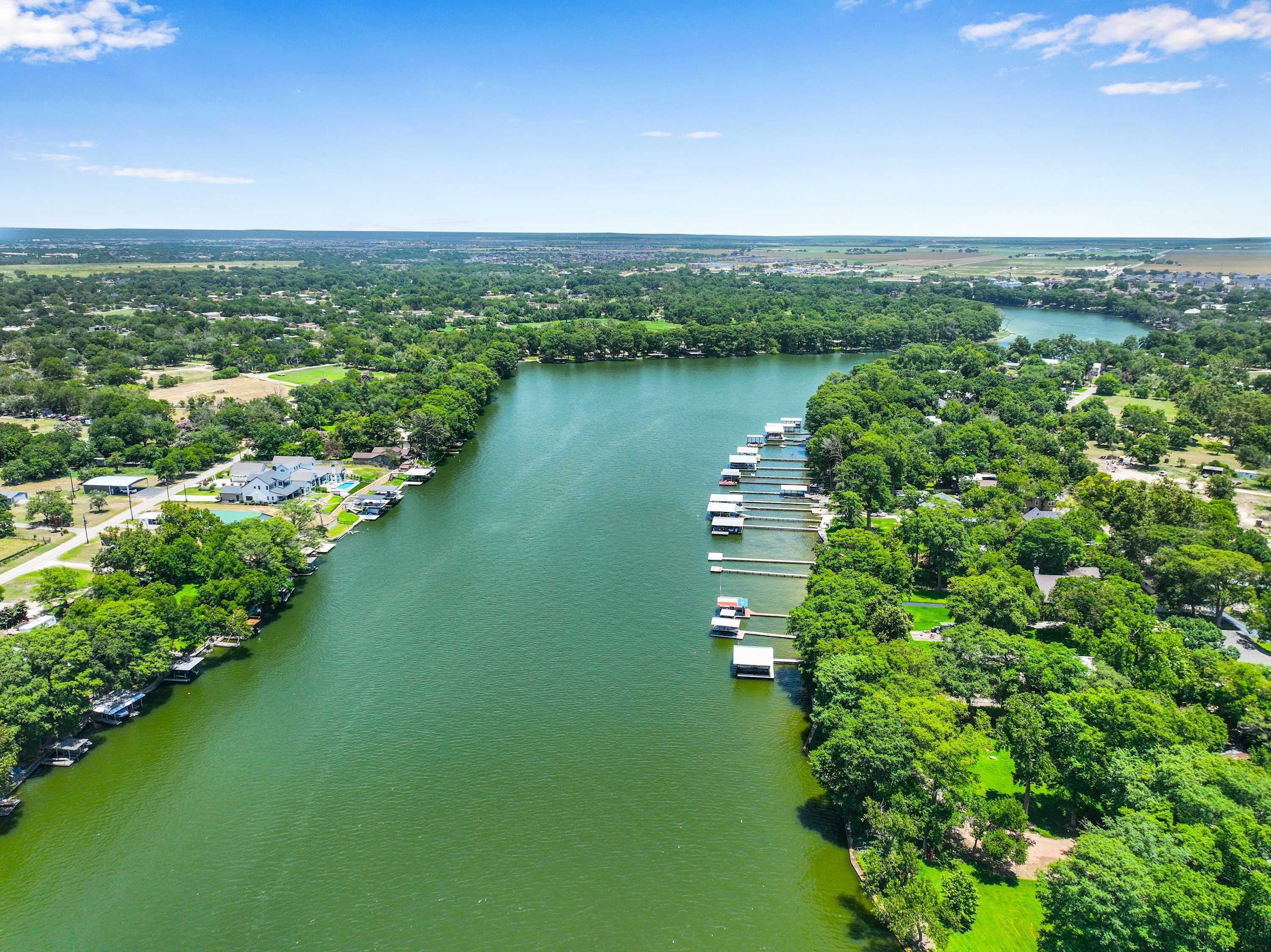 An aerial view of a river with docks and boats, surrounded by greenery and residential areas.