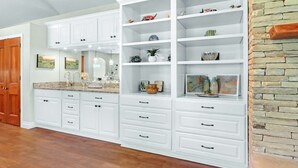 Une cuisine spacieuse avec des meubles blancs, des comptoirs en granit et un mur décoratif en briques.